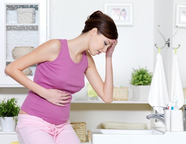 Femme enceinte avec de fortes douleurs d'estomac et des nausées assis dans la salle de bain