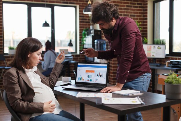 Femme enceinte interrogeant les tableaux de données et les résultats d'analyse commerciale tout en étant assise au bureau. Employé de bureau d'une agence financière informant le responsable du service financier d'une mauvaise stratégie de projet.