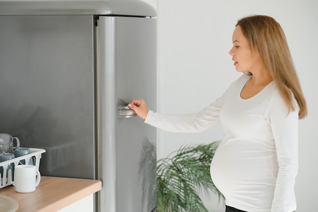 Une femme enceinte à la maison dans la cuisine ouvre le réfrigérateur