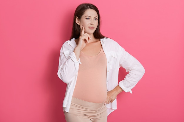 Femme enceinte pensive portant chemise blanche et leggins,