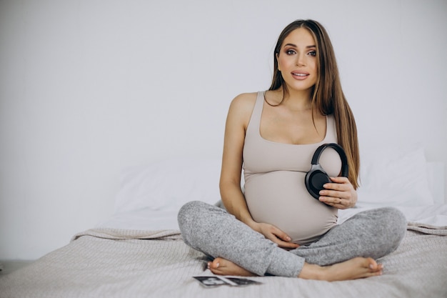 Femme enceinte avec photo échographique mettant des écouteurs avec de la musique sur son ventre