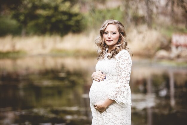 Femme enceinte portant une robe blanche dans un parc avec un lac