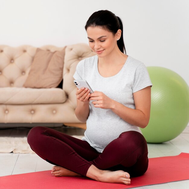 Femme enceinte en position du lotus vérifiant son téléphone