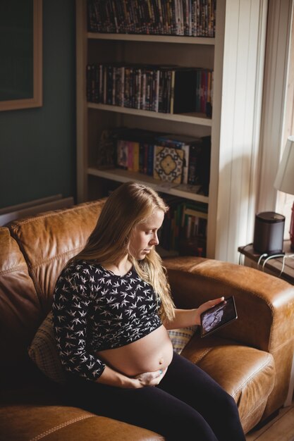 Femme enceinte en regardant une échographie sur une tablette numérique dans le salon