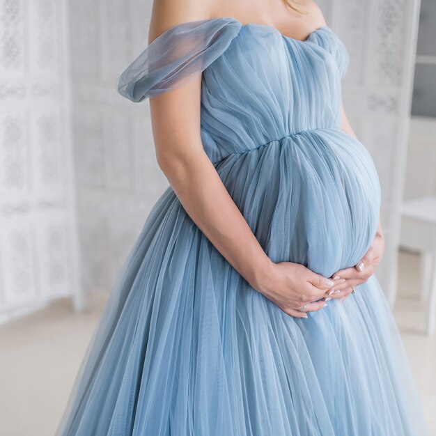 Femme enceinte en robe rose tient les mains sur son ventre