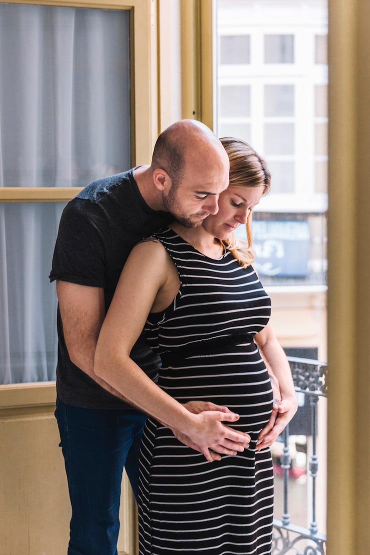 Photo gratuit une femme enceinte et son mari devant la fenêtre.