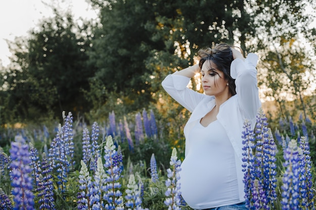 Femme enceinte, stands, parmi, lupins, champ, sur, coucher soleil