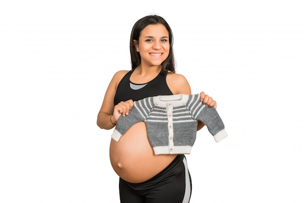 Femme enceinte tenant des vêtements de bébé.