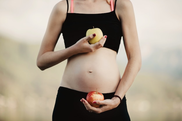 Une femme enceinte en vêtements noirs tient des pommes devant son ventre