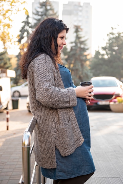 Femme enceinte vue de côté avec une tasse de café en plein air
