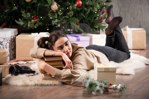 Femme endormie allongée sur un tapis moelleux et étreignant des livres.