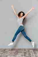 Photo gratuite femme énergique des années 20 en t-shirt rayé et jeans sautant avec les mains jetant en l'air sur gris