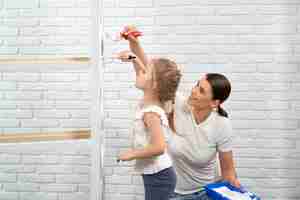 Photo gratuite femme et enfant rafraîchissant les étagères en bois avec de la peinture blanche