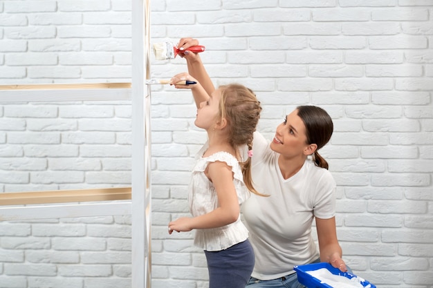 Femme et enfant rafraîchissant les étagères en bois avec de la peinture blanche