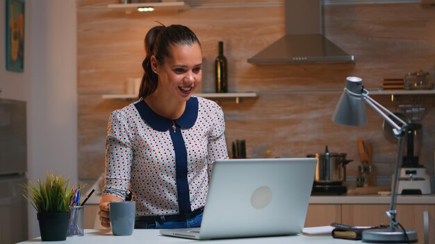 Femme entrepreneur à distance ayant une vidéoconférence avec des collègues utilisant un ordinateur portable assis dans la cuisine tard dans la nuit. Employé occupé utilisant un réseau de technologie moderne sans fil faisant des heures supplémentaires pour son travail.