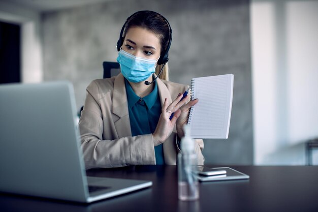 Femme entrepreneur portant un masque facial tout en parlant pendant un appel vidéo au bureau