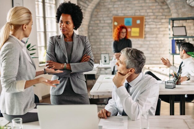 Femme entrepreneure afro-américaine et ses collègues communiquant lors d'une réunion d'affaires dans un bureau moderne Il y a des gens en arrière-plan
