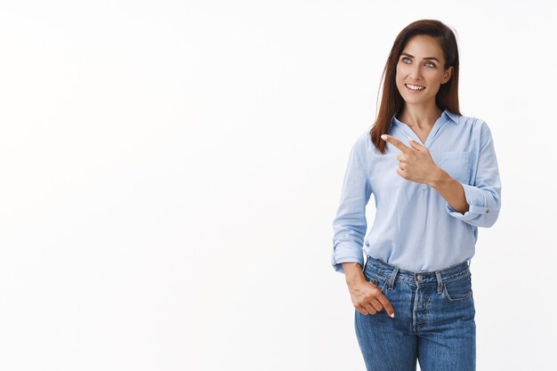 Femme entrepreneure intriguée et confiante, regarde de côté, regard pointé vers la gauche curieuse, comme un bon produit, concept de projet intéressant, stand mur blanc content