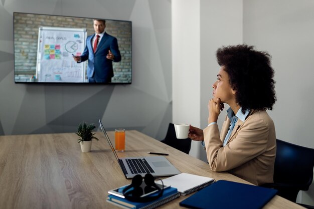 Femme entrepreneure noire écoutant un séminaire d'entreprise en ligne par conférence téléphonique au bureau