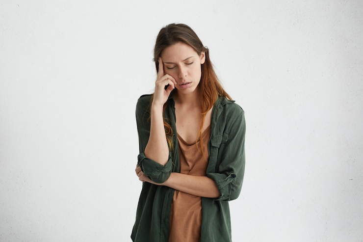 Photo gratuit femme épuisée et fatiguée aux cheveux noirs debout contre un mur blanc avec les yeux fermés tenant l'index sur la tempe en pensant à quelque chose. femme bouleversée avec une expression fatiguée.