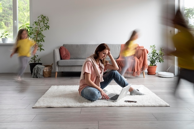 Photo gratuite femme essayant de travailler sur un ordinateur portable à la maison pendant que ses enfants courent partout