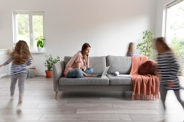 Femme essayant de travailler sur un ordinateur portable à la maison pendant que ses enfants courent partout