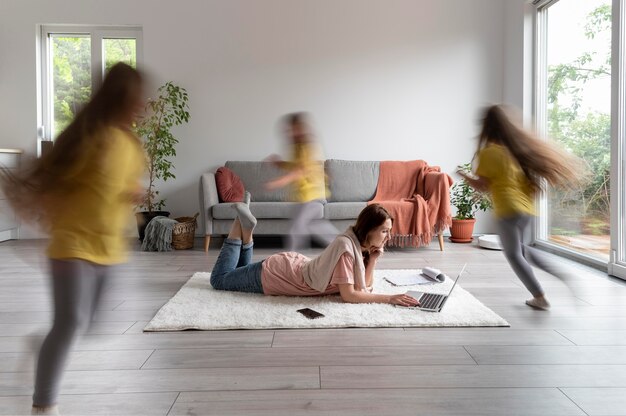 Femme essayant de travailler sur un ordinateur portable à la maison pendant que ses enfants courent partout