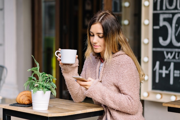 La femme est assise dans la rue et prend son petit déjeuner au soleil