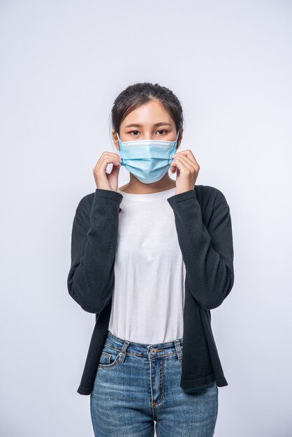 Une femme est malade debout avec un masque. Portez un manteau noir et un jean.