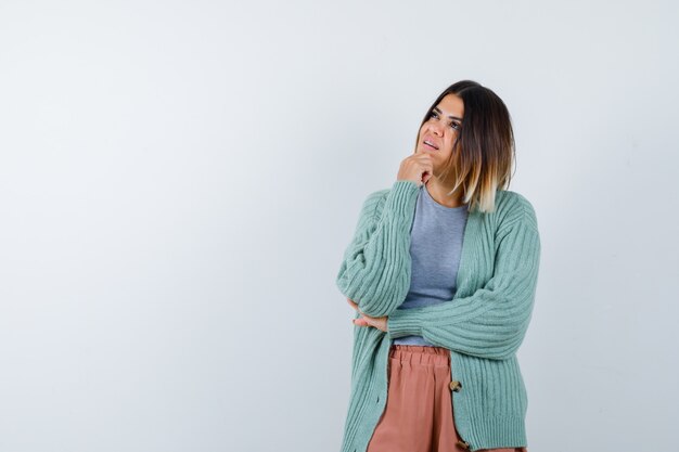 Femme étayant le menton sur place dans des vêtements décontractés et à la recherche pensive, vue de face.