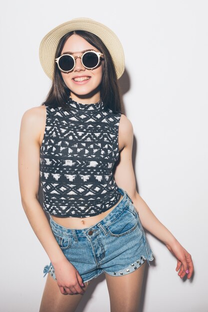 Femme d'été réfléchie en chapeau et lunettes de soleil isolé sur un mur blanc