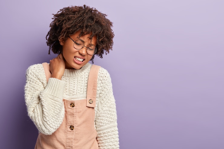 Photo gratuit une femme ethnique bouleversée ressent une douleur terrible dans le cou après une chute d'escalier, grimace de sentiments douloureux, a des problèmes de santé et des douleurs dans la colonne vertébrale, a un mode de vie sédentaire, isolé sur violet