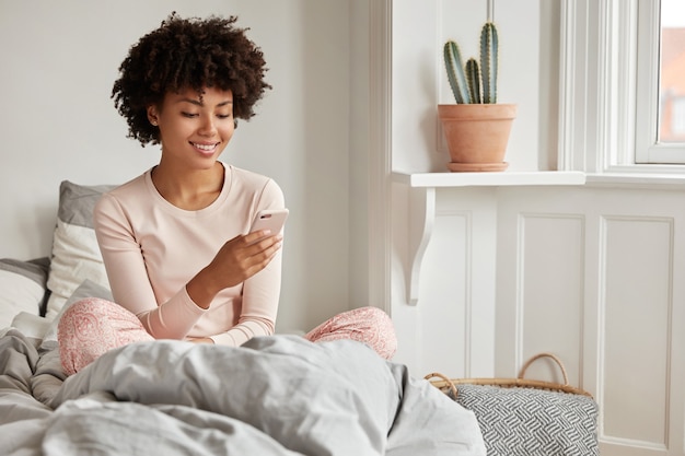 Une femme ethnique heureuse envoie un message via un téléphone intelligent contemporain