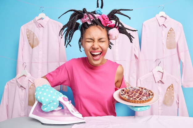 Une femme ethnique joyeuse et multitâche repasse des vêtements