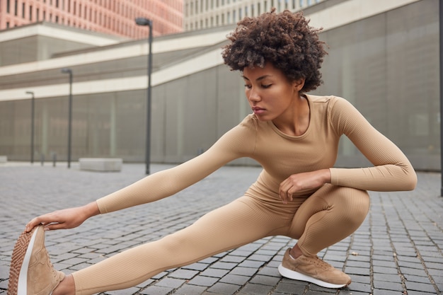 la femme étire ses ischio-jambiers pose en plein air porte des vêtements de sport beiges et des baskets fait de l'exercice en bonne forme physique