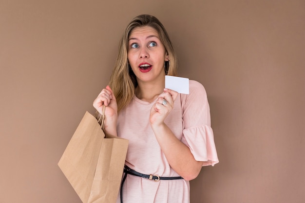 Femme étonnée debout avec sac à provisions et carte de crédit
