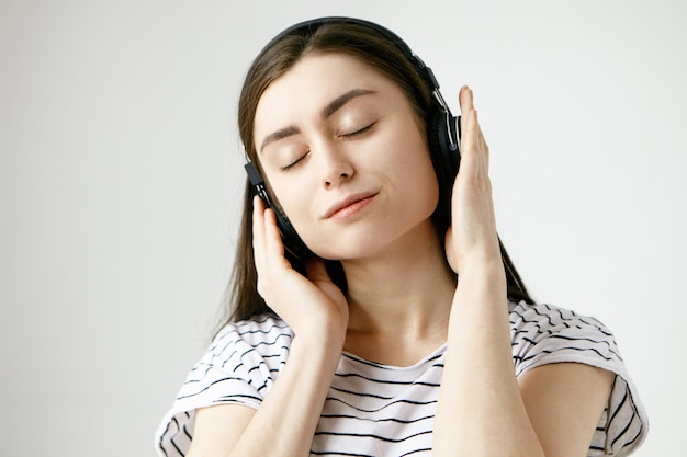 Femme étudiante brune posant les yeux fermés, écoutant des sons méditatifs calmes de la nature ou des pistes ambiantes à l'aide d'un casque