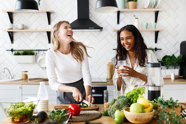 Une femme européenne coupe un concombre et une femme africaine boit du lait, ils rient