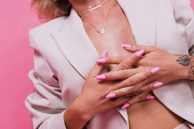 Femme européenne élégante en élégant blazer beige et bijoux dorés, ongles vernis en gel rose vif, posant