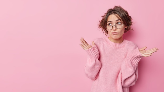 Une Femme Européenne Hésitante Avec Une Coiffure Bob à La Mode écarte Les Paumes Sur Le Côté Se Sent Désemparée Ne Peut Pas Prendre De Décision Habillée Avec Désinvolture Pose Sur Fond Rose Espace Vide à Gauche Pour La Publicité