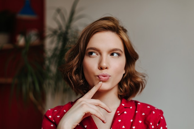 Femme européenne pensive en vêtements de nuit à la recherche de suite. Tir intérieur d'une jolie femme bouclée en pyjama rouge.