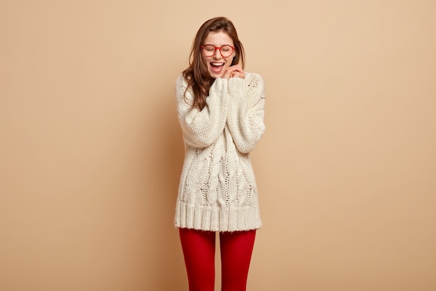 Une femme européenne ravie de rire sincèrement, garde les mains jointes près du visage, garde la bouche ouverte, heureuse des nouvelles positives