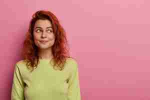 Photo gratuite femme européenne rousse pensif conscient en pull vert, regarde de côté sur un espace vide, pense quoi faire, se souvient de quelque chose
