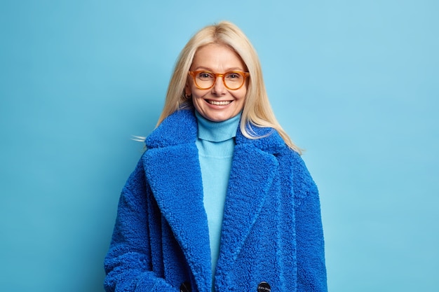 Une Femme Européenne Souriante Aux Cheveux Blonds Vêtue D'un Manteau D'hiver Bleu A Une Bonne Humeur Porte Des Lunettes.