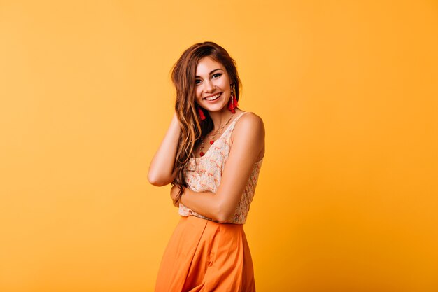 Femme européenne timide en vêtements jaunes posant en studio avec un sourire sincère. Modèle féminin aux cheveux roux spectaculaire exprimant le bonheur.