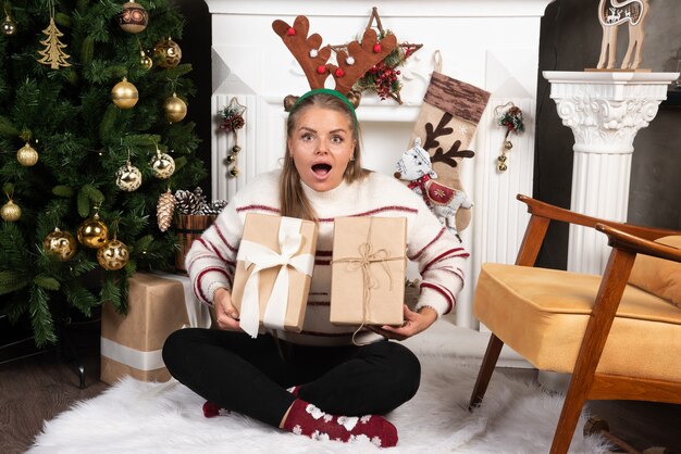 Une femme excitée dans des oreilles de cerf tenant deux cadeaux de Noël.
