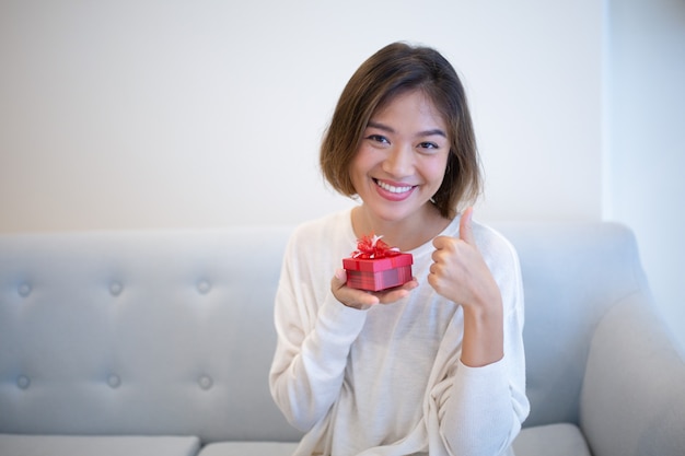 Femme excitée positive avec petite boîte-cadeau montrant le pouce en l&#39;air