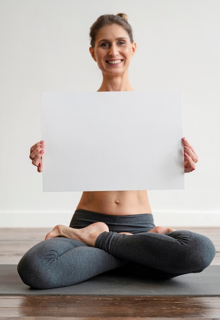 Photo gratuite femme exerçant le yoga et tenant une pancarte vierge