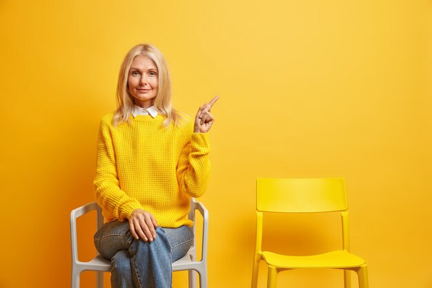 une femme à l'expression calme porte un pull et un jean pose sur une chaise indique en haut à droite seule passe du temps seule