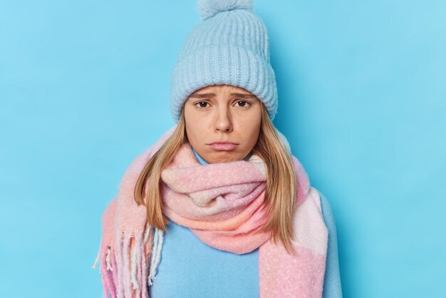 la femme a une expression sombre alors que quelqu'un blesse ses sentiments se plaint de quelque chose porte un bonnet tricoté et une écharpe autour du cou isolé sur bleu se sent coupable